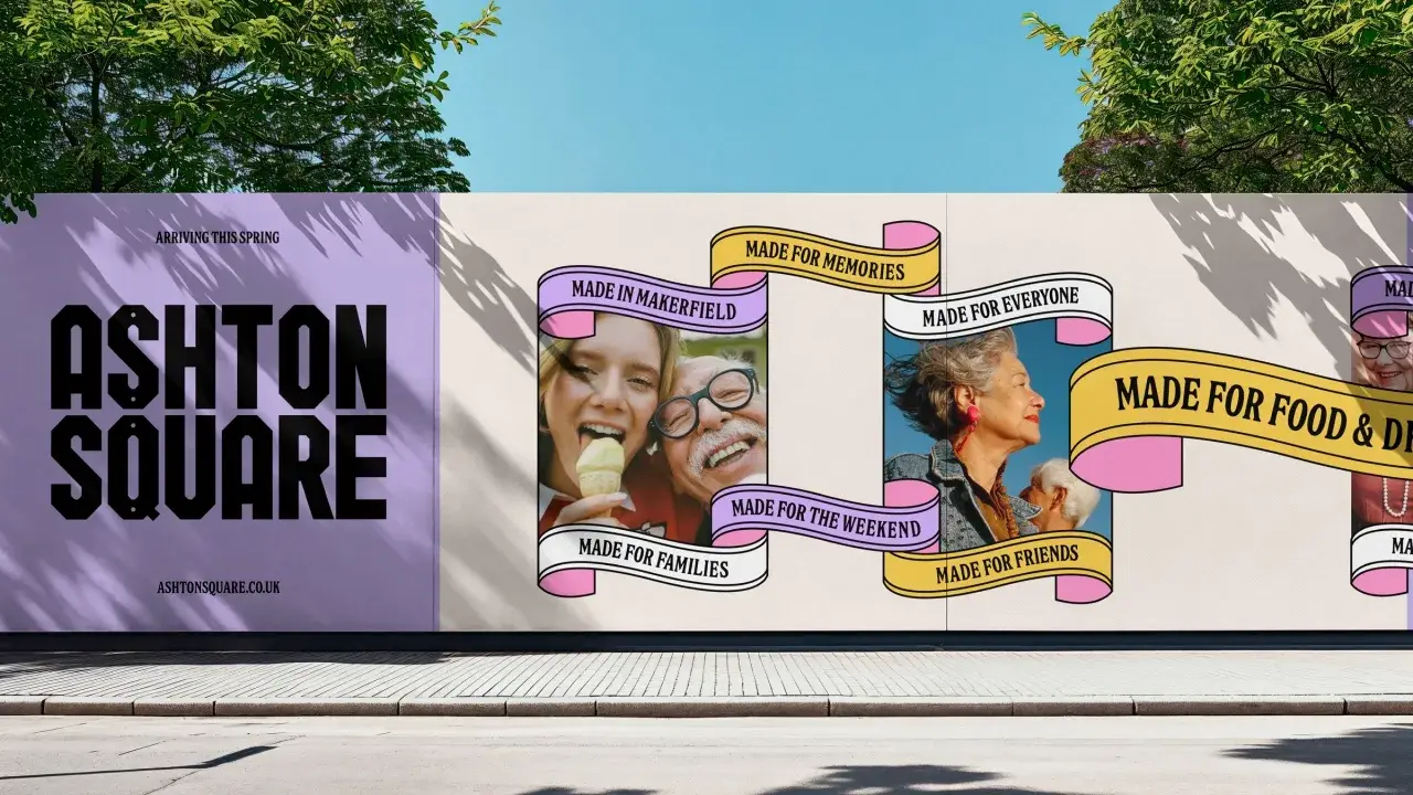 Ashton Square construction hoarding: massive black letterforms on lilac, with pink and yellow ribbons reading Made in Makerfield, Made for Memories, Made for Everyone