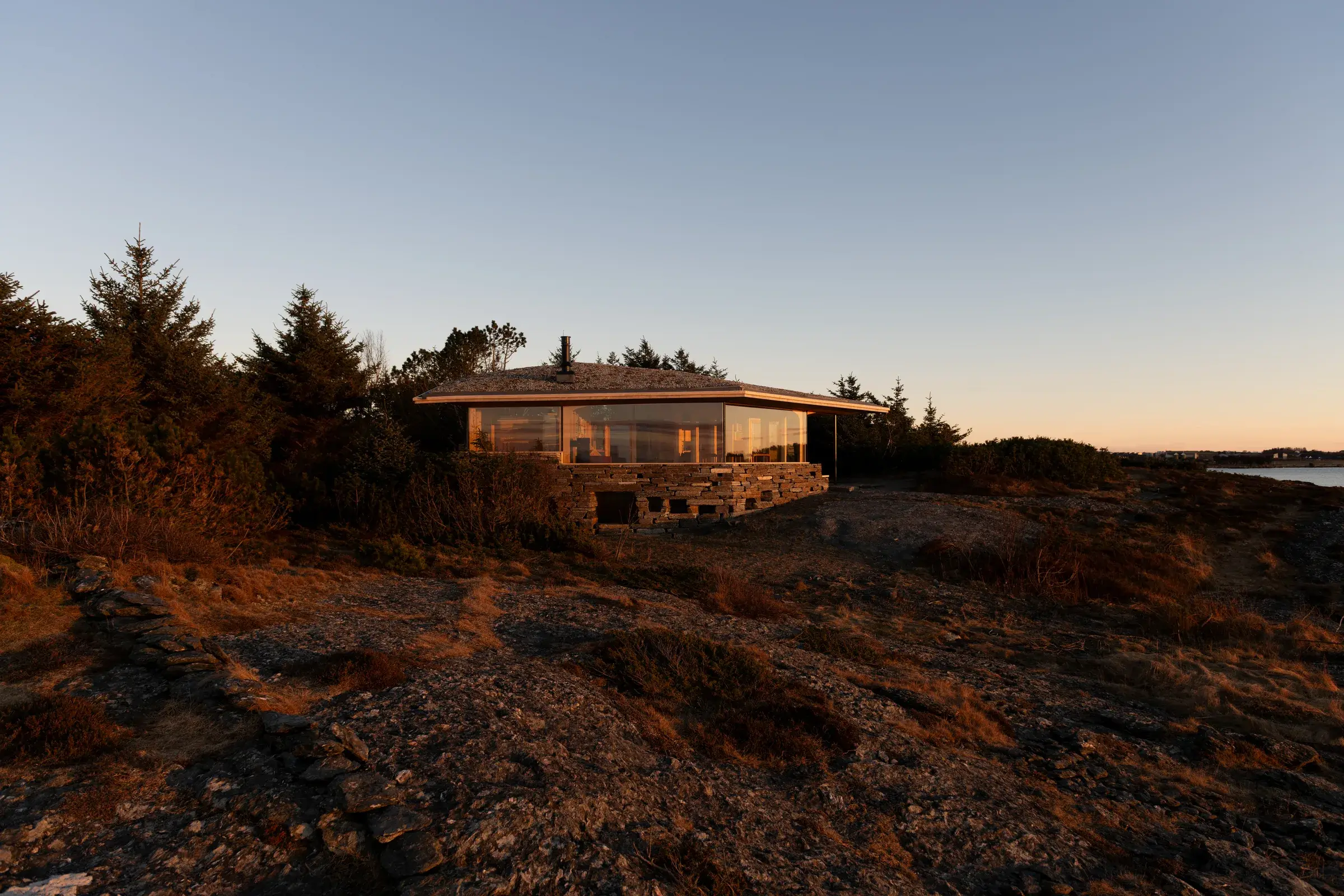 Cabin Sande, a low timber-and-glass silhouette set against a rocky headland on the Atlantic coast