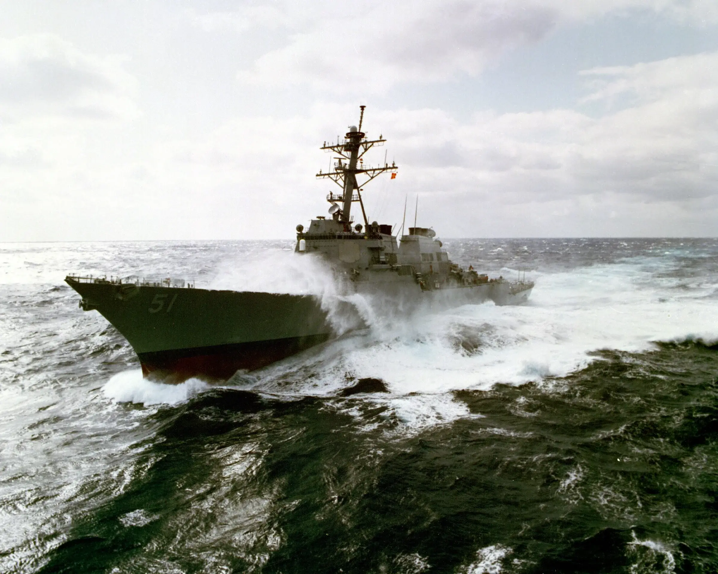 The destroyer USS Arleigh Burke (DDG-51) underway in heavy seas, its mast crowded with antennas and radars visible above the superstructure