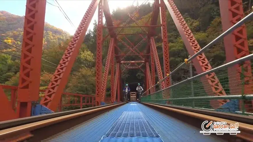 Two riders cross the red bridge over the second Takahara river on an electric rail bike, in the Urushiyama gorge