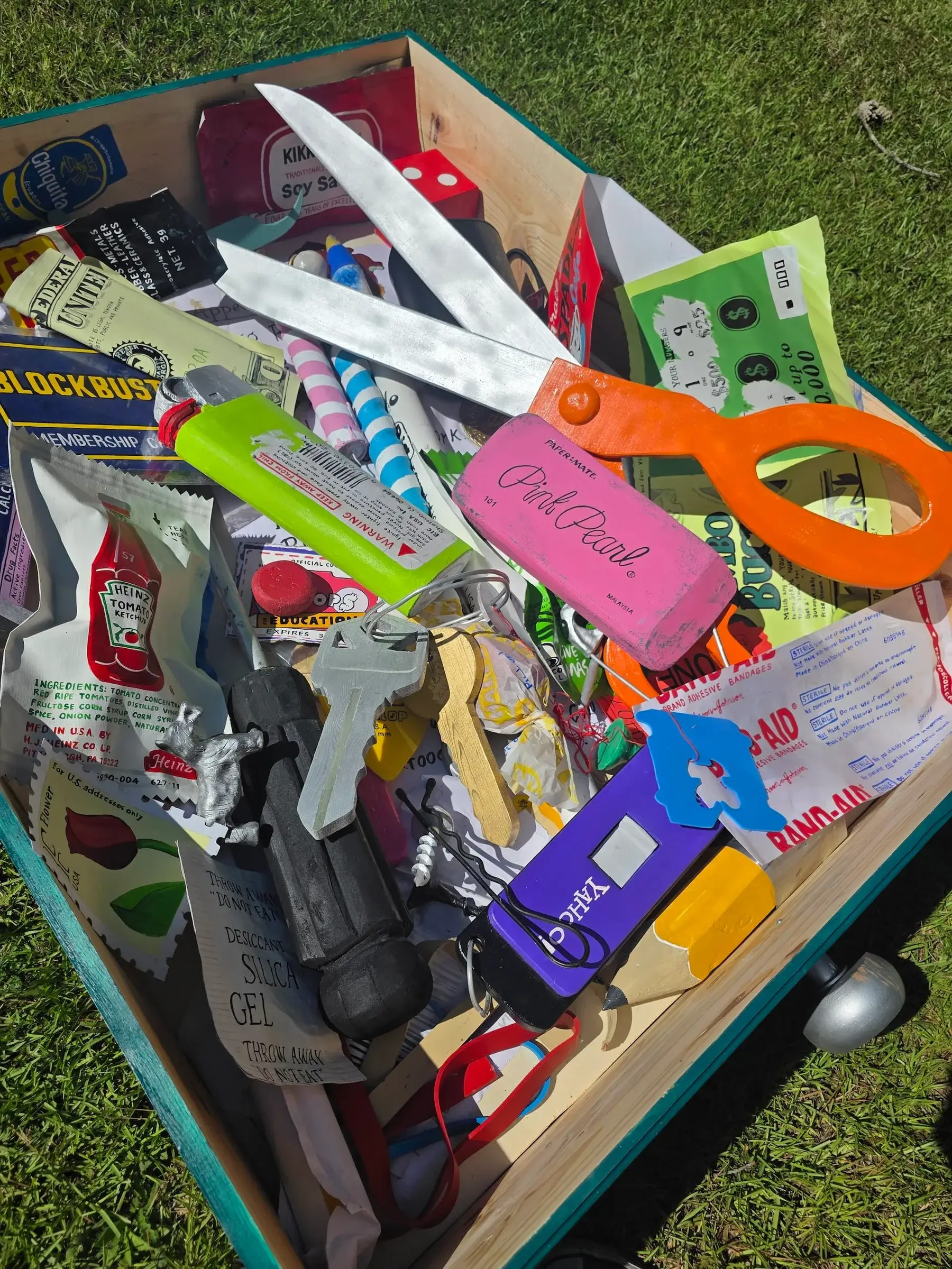 Overhead view of the giant junk drawer filled with handmade objects: scissors, a Pink Pearl eraser, a ketchup packet, a bandage box, keys, a lighter