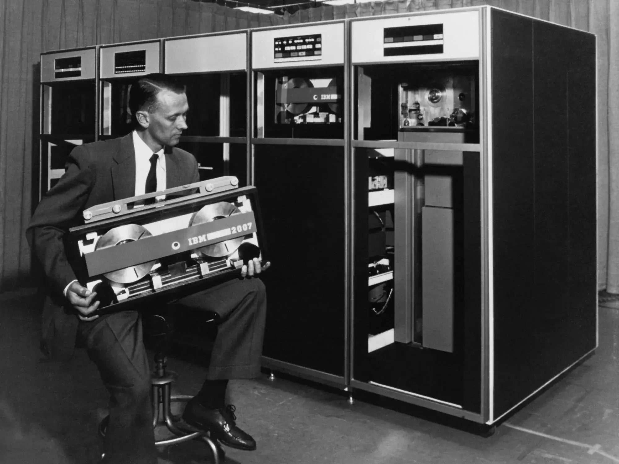 An IBM technician holds a Tractor tape cassette in front of drive cabinets
