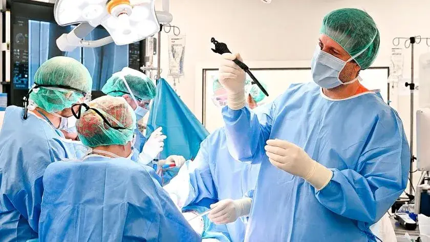 Un chirurgien du bloc opératoire soulève entre ses doigts gantés la prothèse de tibia en treillis de titane ajouré