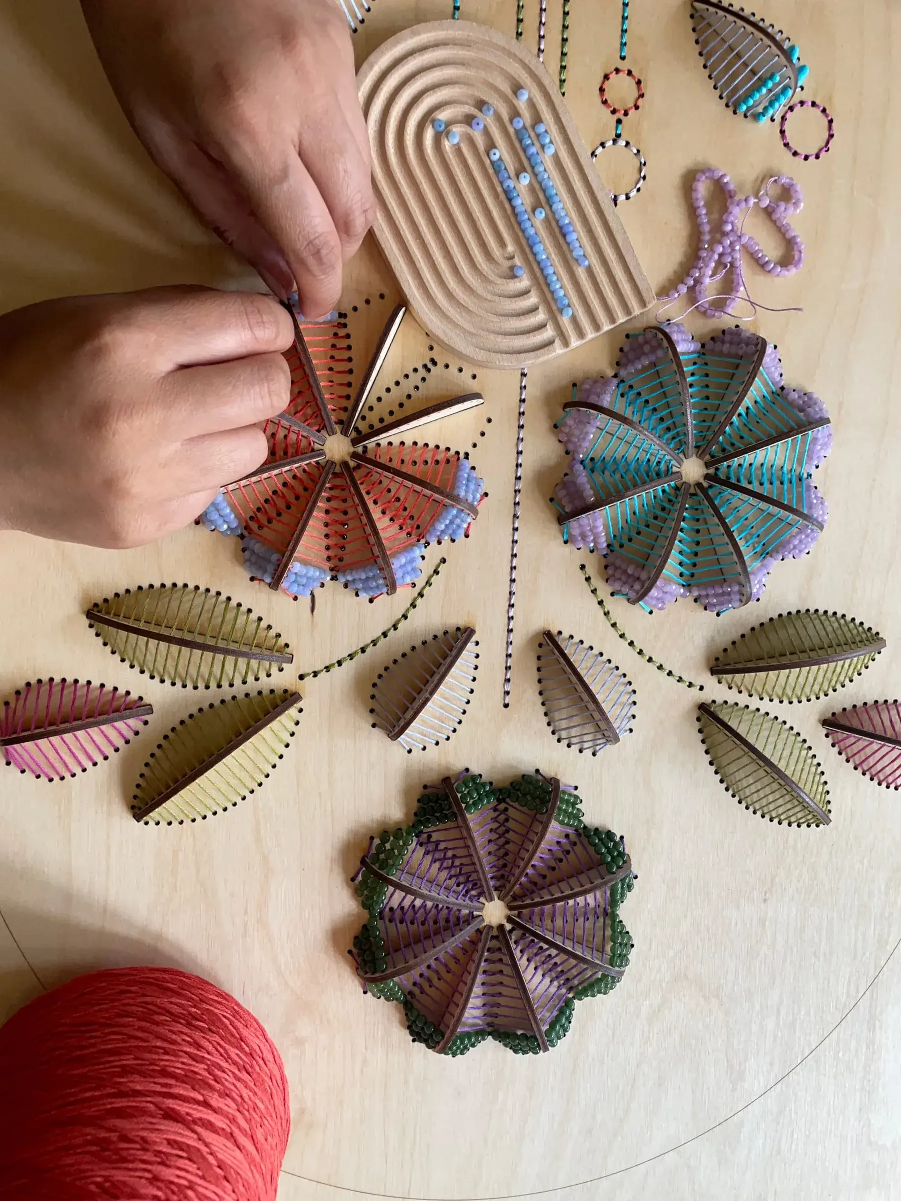Mains en train de broder du fil rouge et bleu à travers un panneau de bois percé de trous, pétales de fleurs sculpturales en cours
