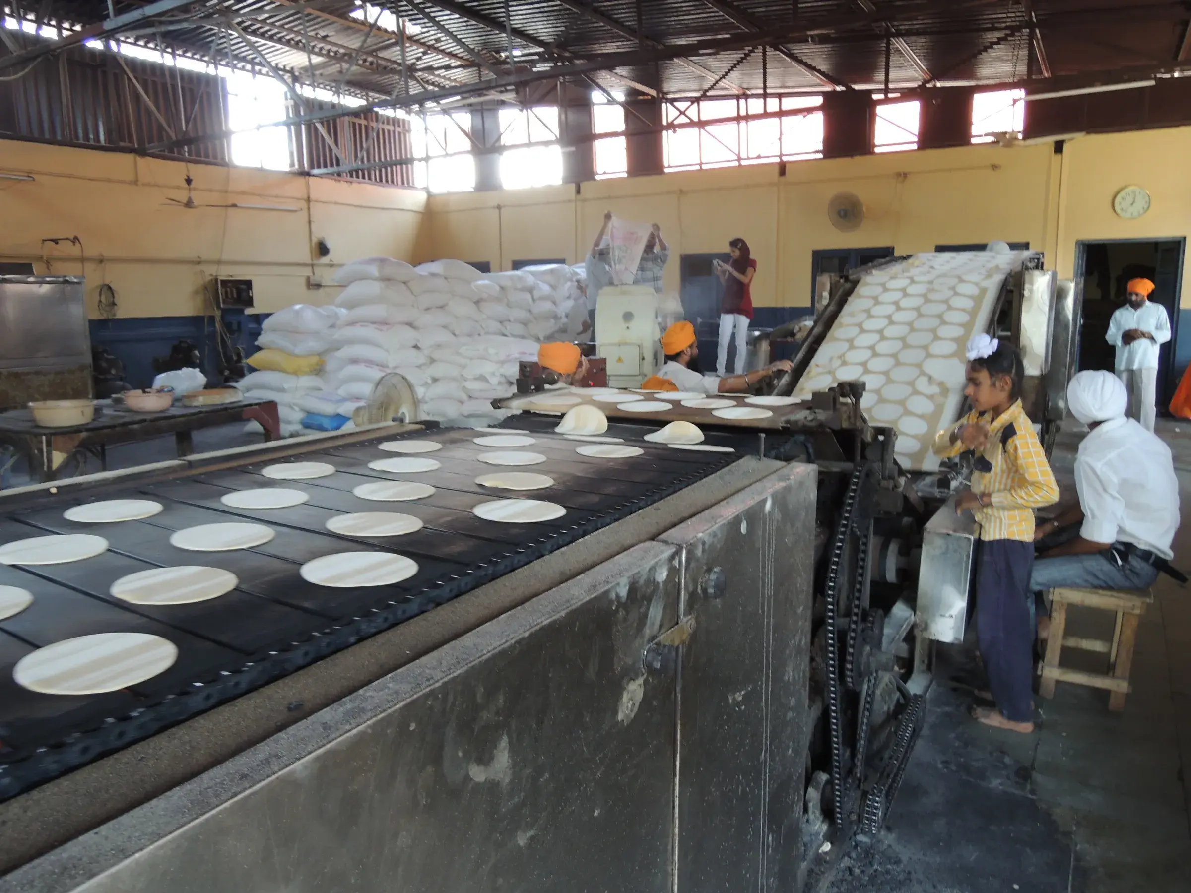 Automatic chapati machine at work in the langar of the Golden Temple in Amritsar, with cooked discs lined up on a conveyor