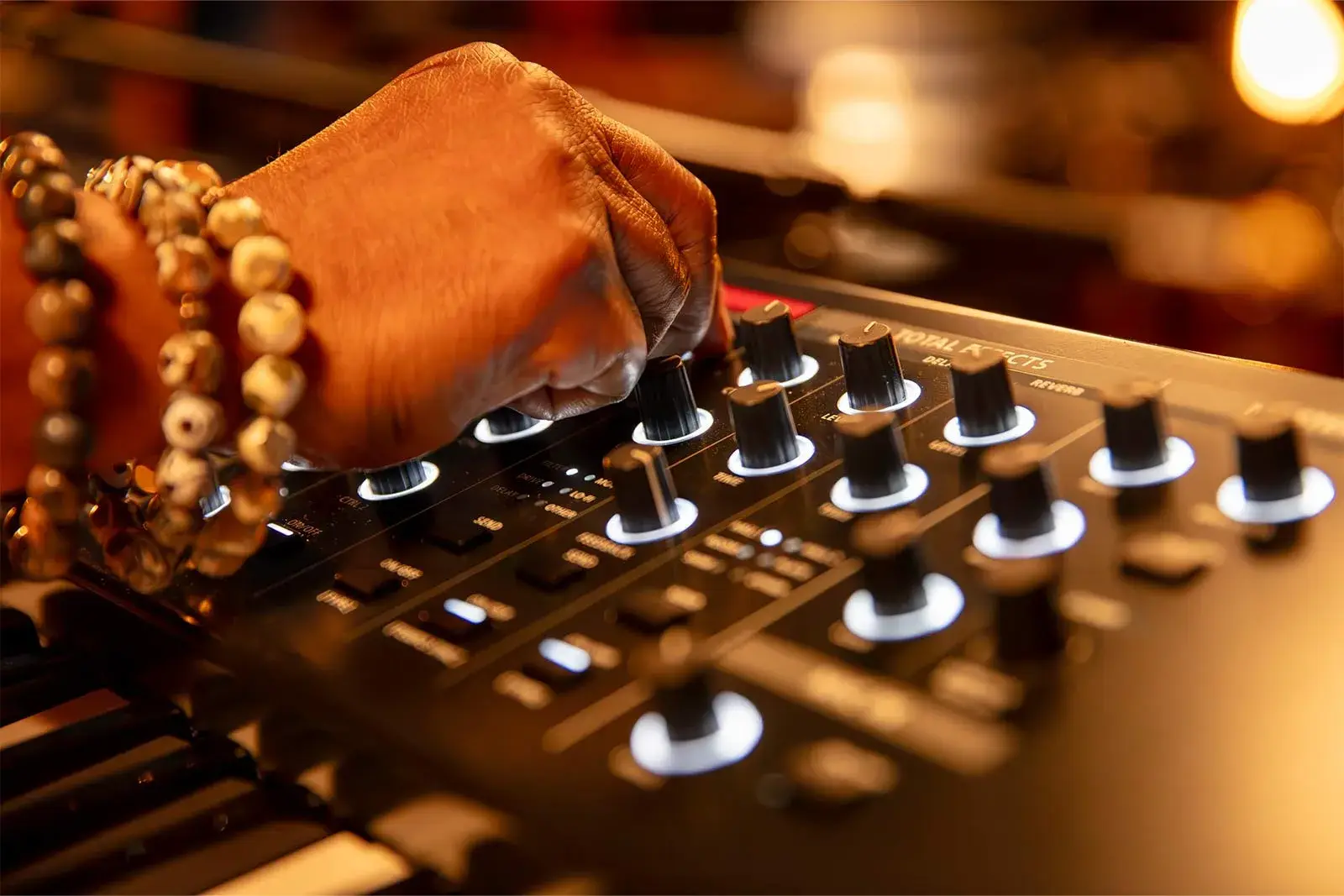 Main manipulant une rangée de potentiomètres physiques sur le panneau du Roland V-STAGE