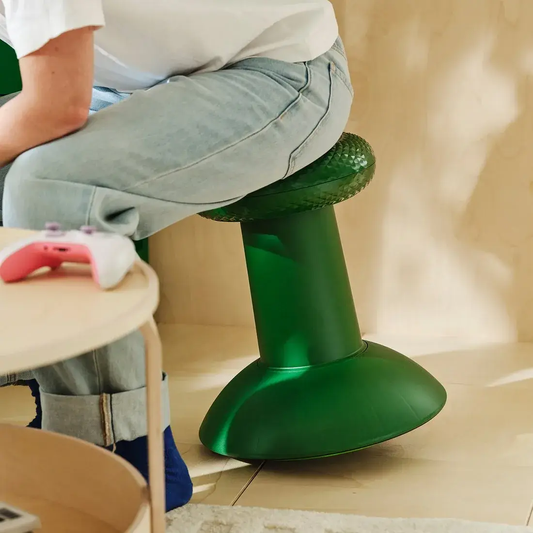 Personne assise sur le tabouret YXSTABY vert, une manette Xbox posée à côté